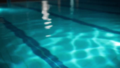 The interior of a quiet indoor swimming pool with soft blue-tinted light and calm water